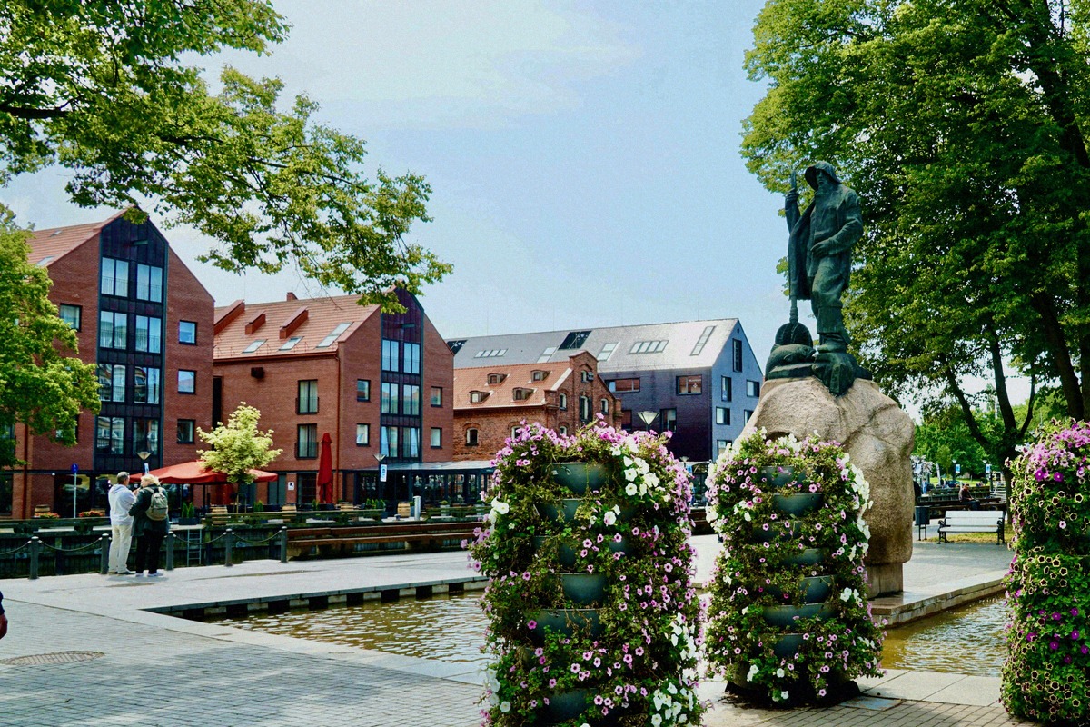 Die Danė-Promenade in Klaipėda mit Fischer-Skulptur und Speicherhäusern.
