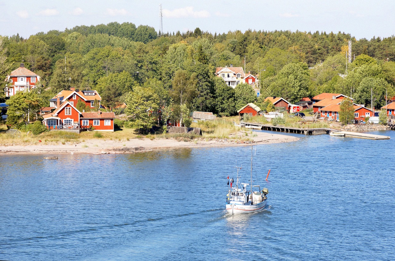 Fischerboot kehrt in den Hafen Grisslehamn zurück, dahinter rote Holzhäuser